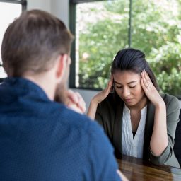 An upset woman, with her head in her hands, discusses issues with an attentive male counselor.