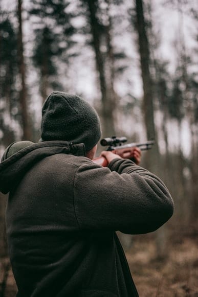 hunting-behind-hearing-loss Backside of man holding and pointing a rifle in a forest.