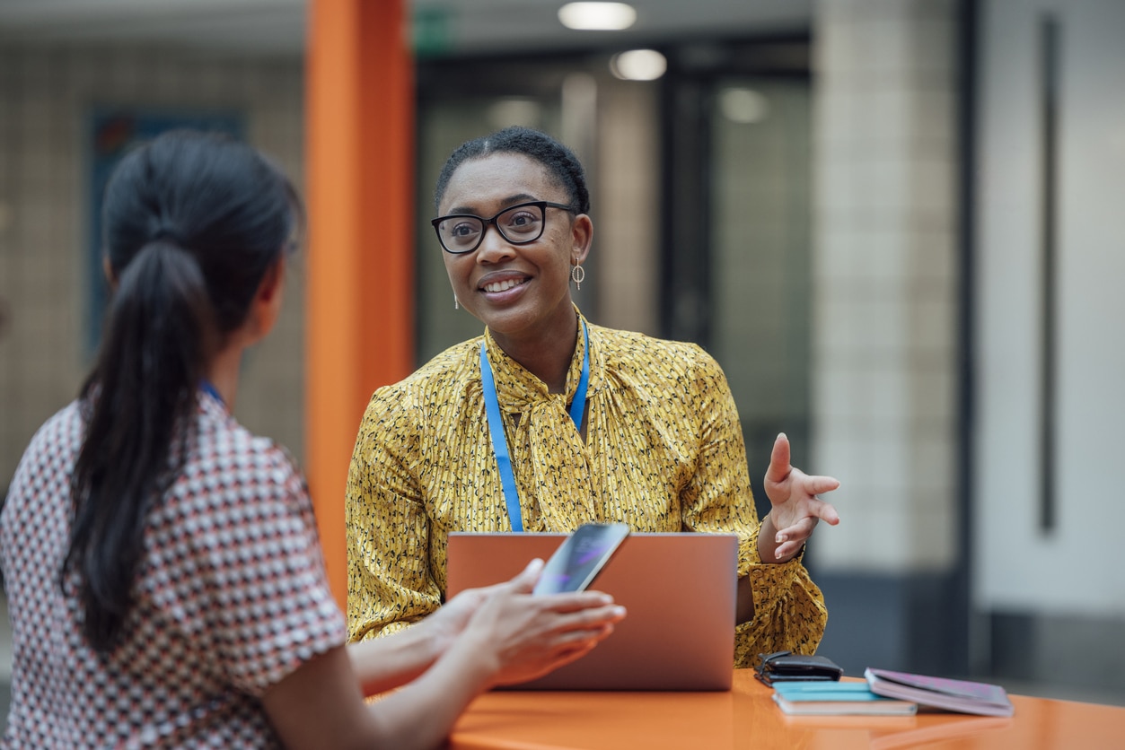 Two women having a conversation at a desk.