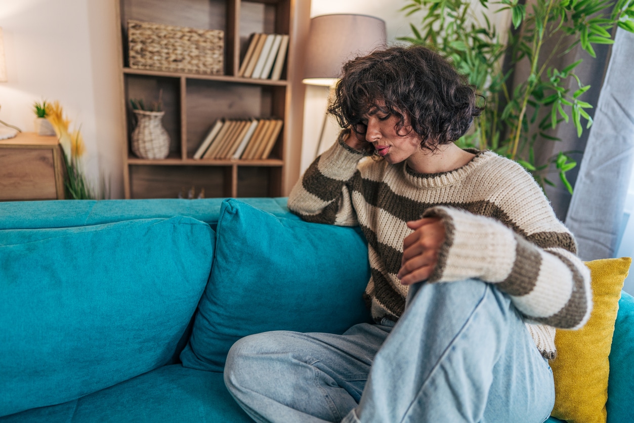 Woman sitting on a couch holding her pounding head.