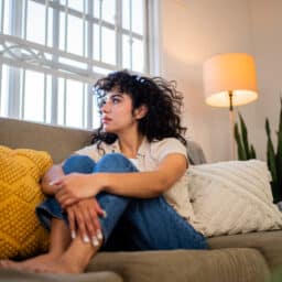 Young woman looking through the window at home, looking sad