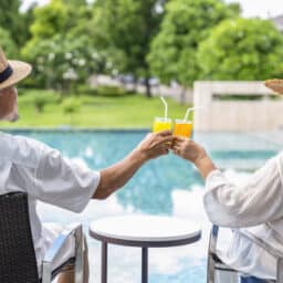Senior couple sitting by the pool and clinking glasses.