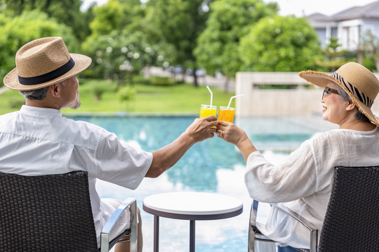 Senior couple sitting by the pool and clinking glasses.